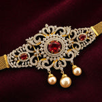 Gold-plated filigree bridal collar necklace with red gemstone accents and dangling pearl beads, displayed on a deep burgundy velvet background.