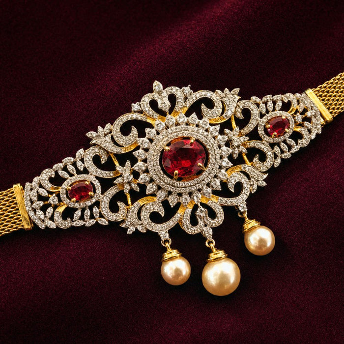 Gold-plated filigree bridal collar necklace with red gemstone accents and dangling pearl beads, displayed on a deep burgundy velvet background.