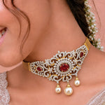 An ornate choker necklace worn by a model, featuring a gold mesh base, intricate silver filigree, red gemstone accents, and three dangling white pearls.