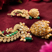 Two ornate gold-toned jhumka earrings with green and white stones, displayed on a deep burgundy velvet background.
