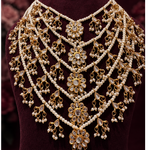 An ornate gold and white pearl choker necklace displayed on a dark burgundy velvet jewelry bust, set against a dark maroon background.