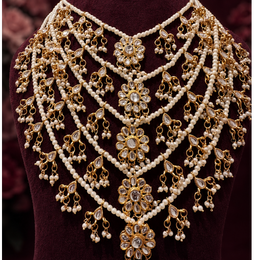 An ornate gold and white pearl choker necklace displayed on a dark burgundy velvet jewelry bust, set against a dark maroon background.