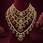An ornate gold-toned traditional necklace with multiple strands of white pearls and intricate floral motifs, displayed on a dark red velvet jewelry bust.