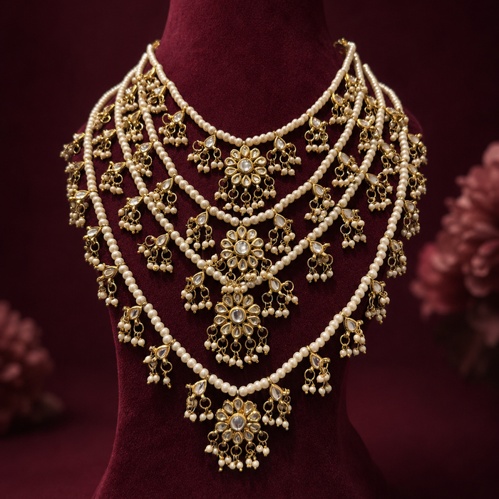 An ornate gold-toned traditional necklace with multiple strands of white pearls and intricate floral motifs, displayed on a dark red velvet jewelry bust.