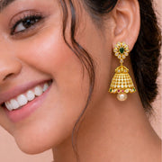 A close-up of a woman wearing a gold-toned traditional Indian jhumka earring with green, red, and white stones, and a pearl drop, shown on her ear.