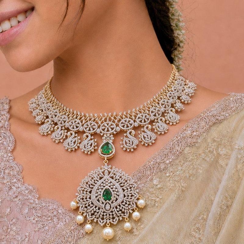 A close-up of a woman wearing an ornate gold and white stone choker necklace with a large matching pendant featuring green emerald accents and pearl-like drops, paired with a beige embroidered saree.